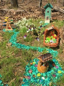 A bejeweled two story fairy house, a tiny fairy wheel, a Fairy Farmer's Market and the Wishing Well nestled among white and purple flowers.